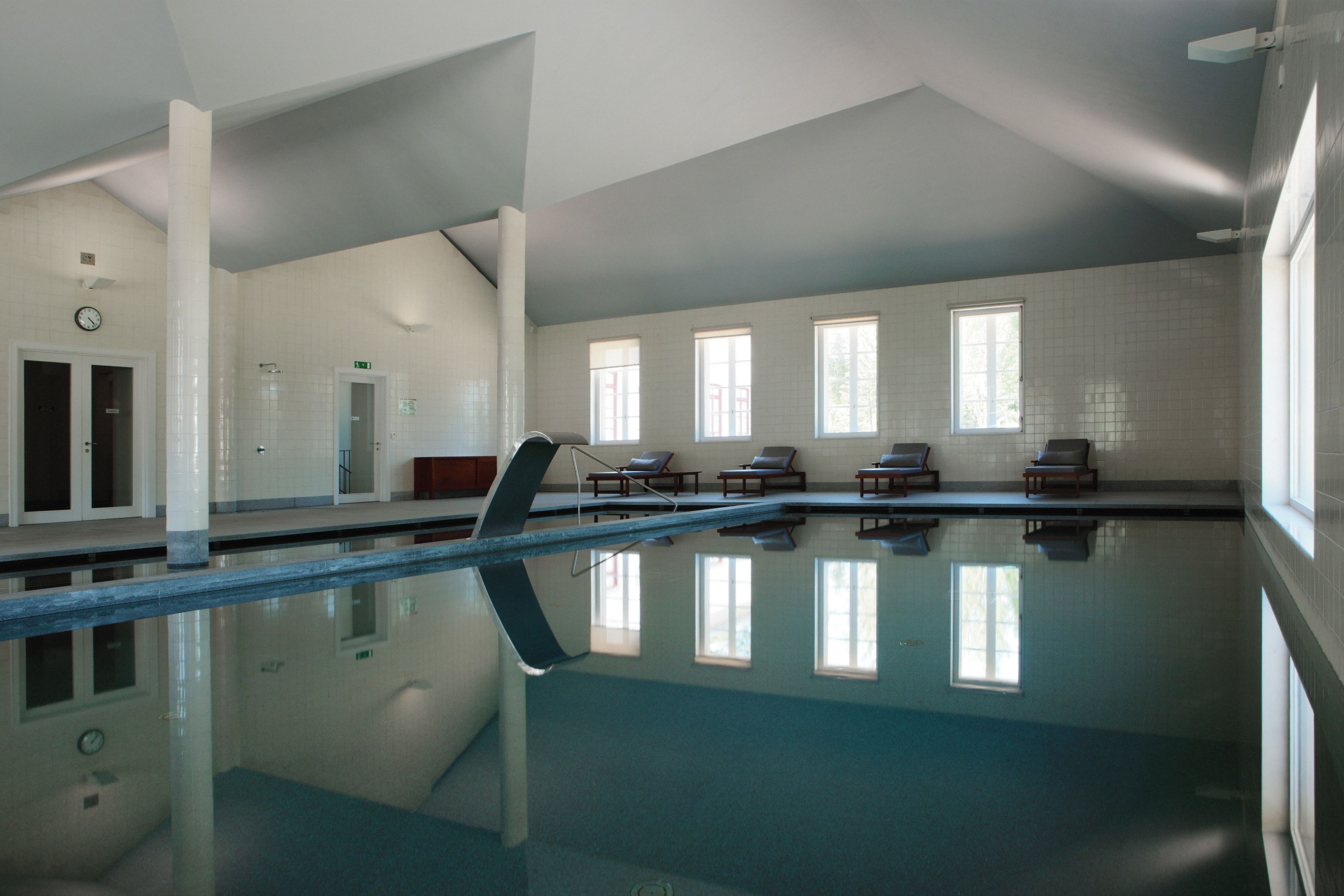 A large indoor swimming pool with clear water, sunlit windows, and lounge chairs along the side.