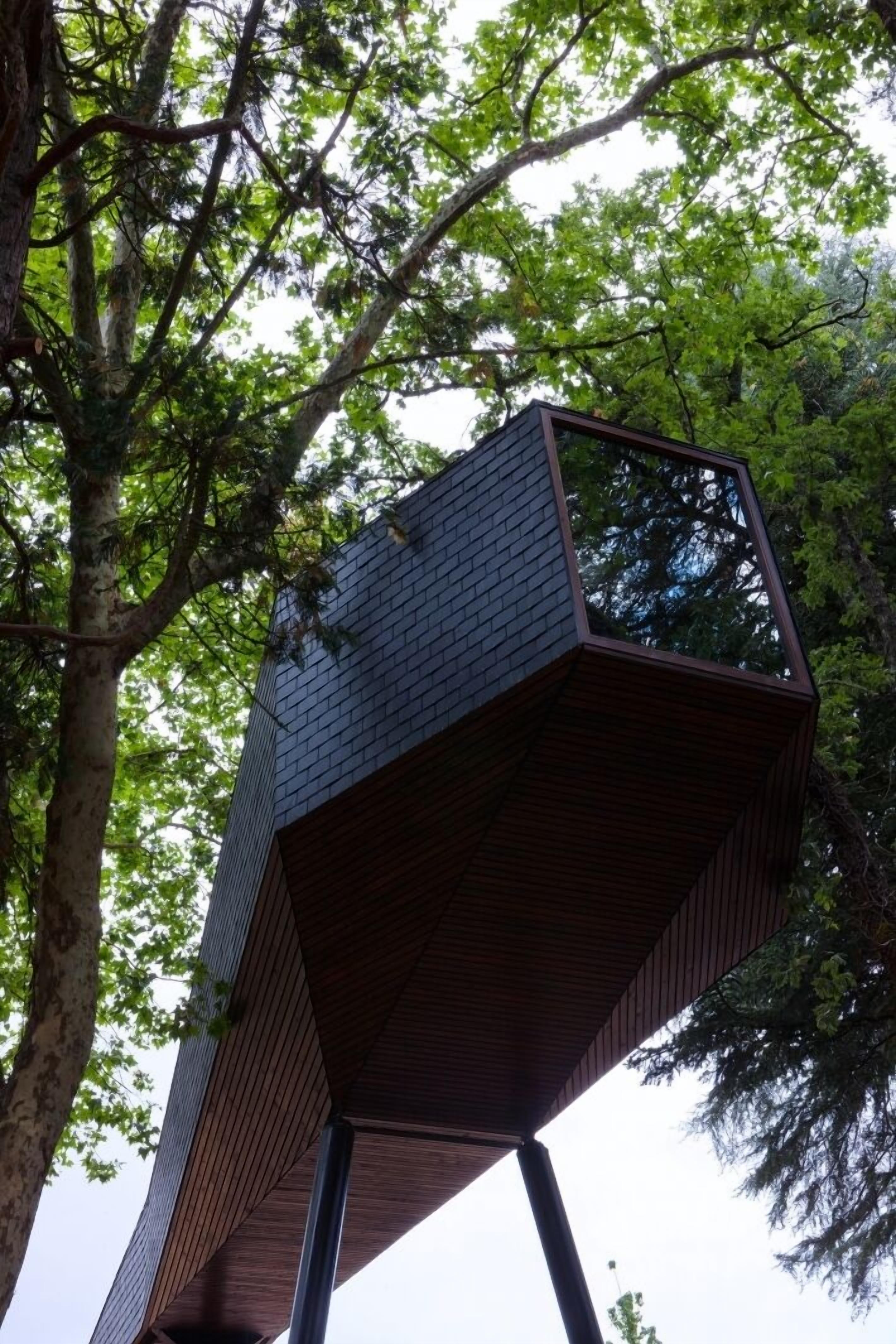 Uma estrutura moderna de casa na árvore com design geométrico e telhado inclinado, cercada por árvores verdes exuberantes.