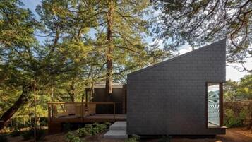 Una cabaña moderna y minimalista con techo inclinado, rodeada de un bosque denso.