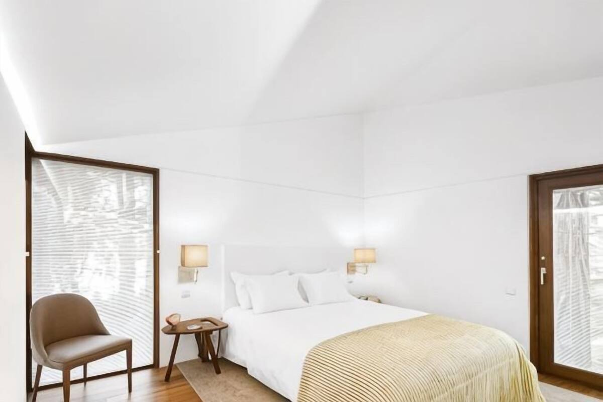 A hotel room with a bed, a chair, a nightstand, and two wall-mounted lamps.