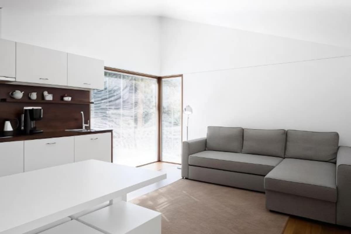 Una cocina moderna con armarios blancos, un sofá gris y un ventanal grande.