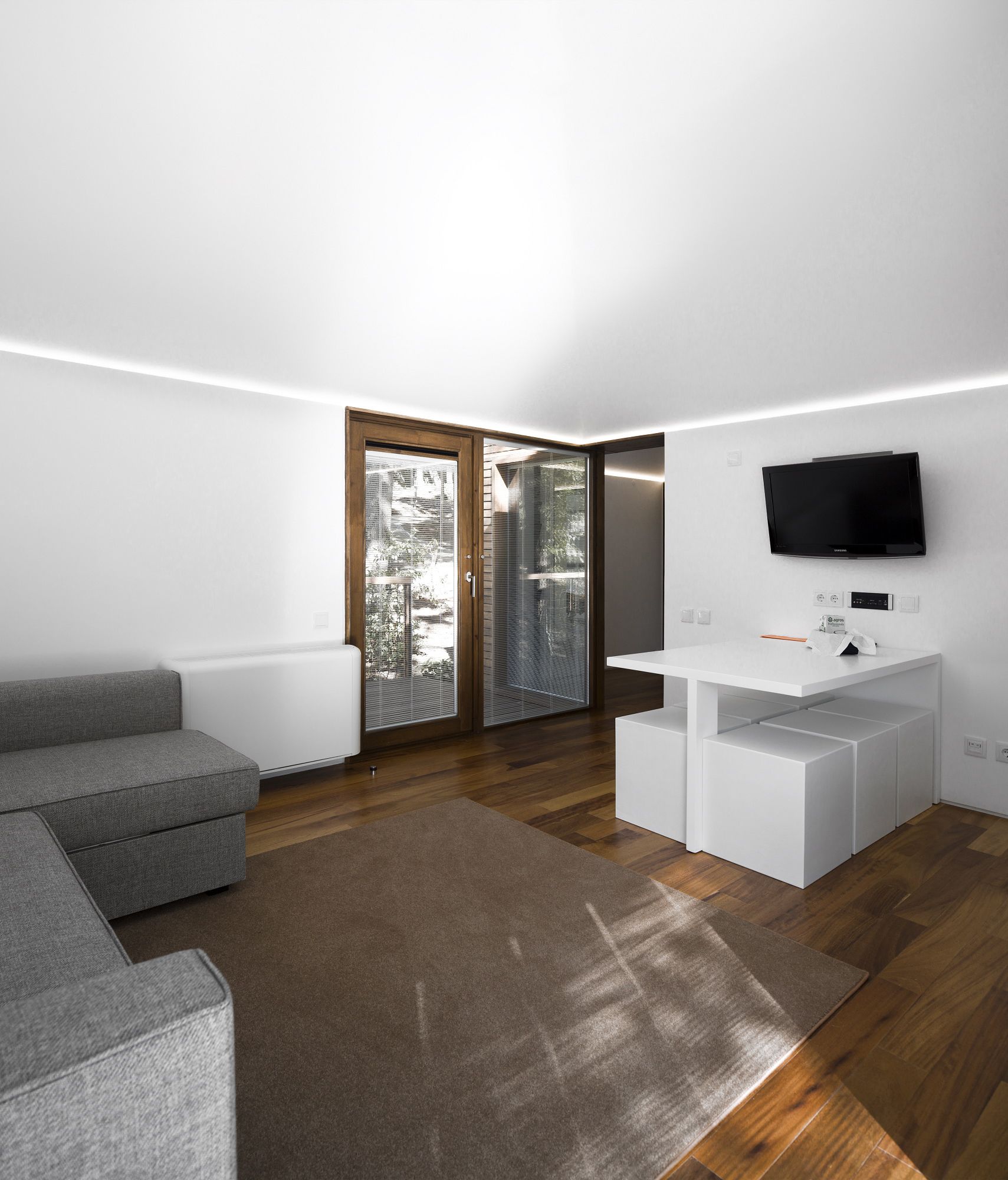 Una sala moderna con un sofá gris, un mueble blanco para entretenimiento y un televisor de pantalla plana montado en la pared.