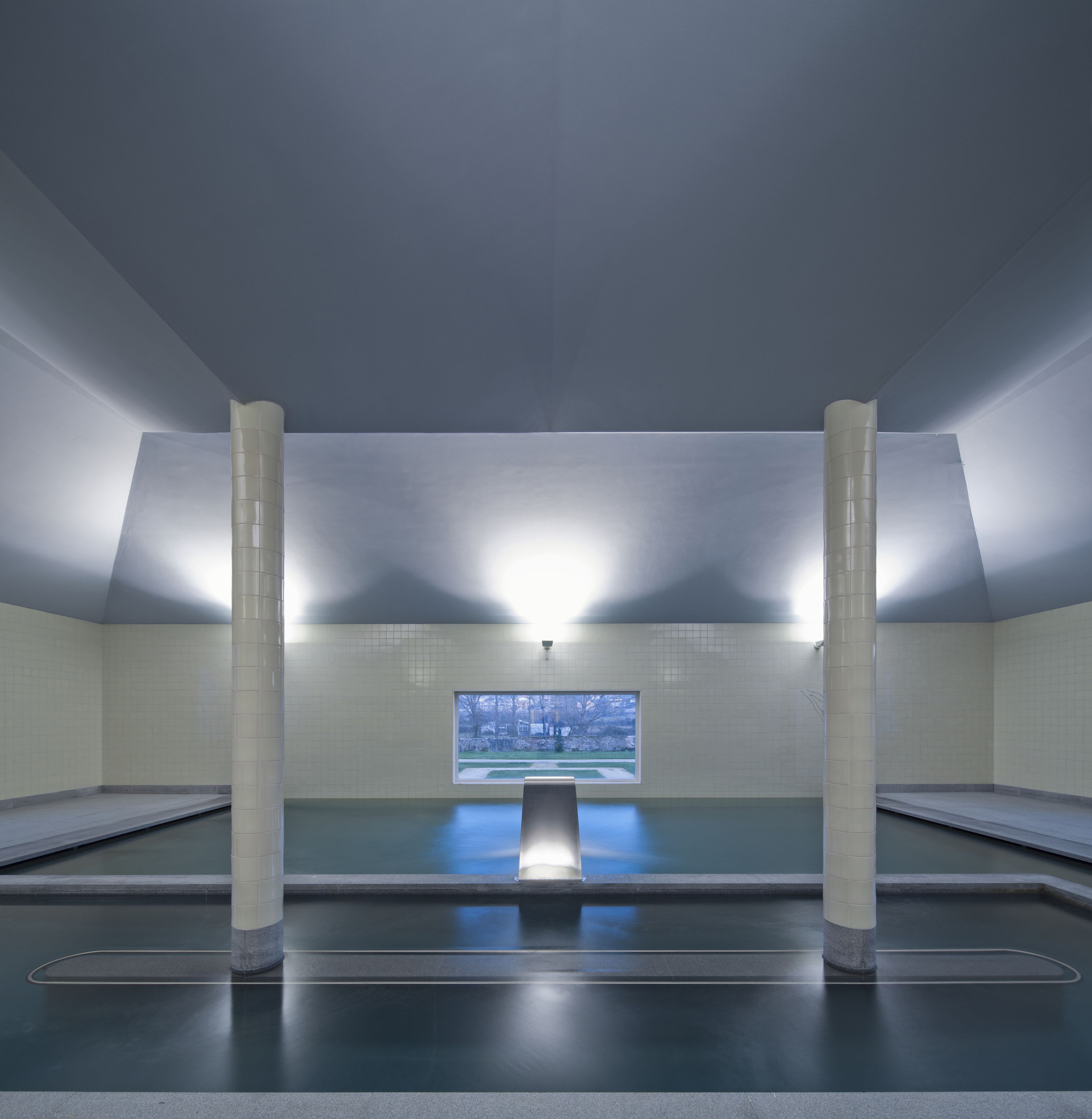 Una piscina moderna y vacía con una pantalla digital y vistas a un jardín.