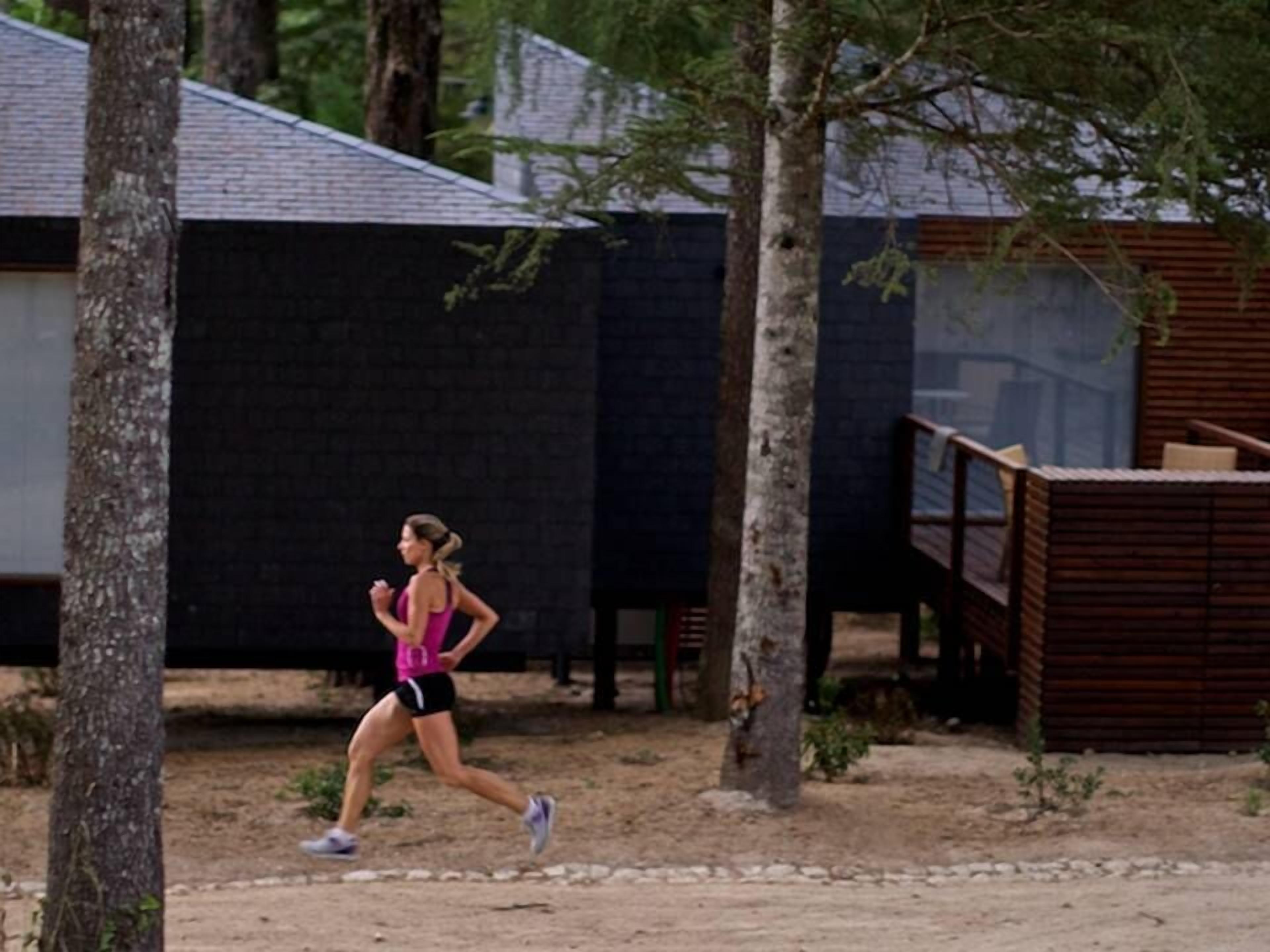 Una persona corre per un camí de terra, amb arbres i un edifici al fons.