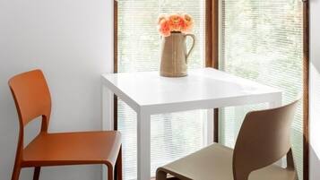 Una pequeña mesa con un florero, dos sillas y una ventana con persianas.