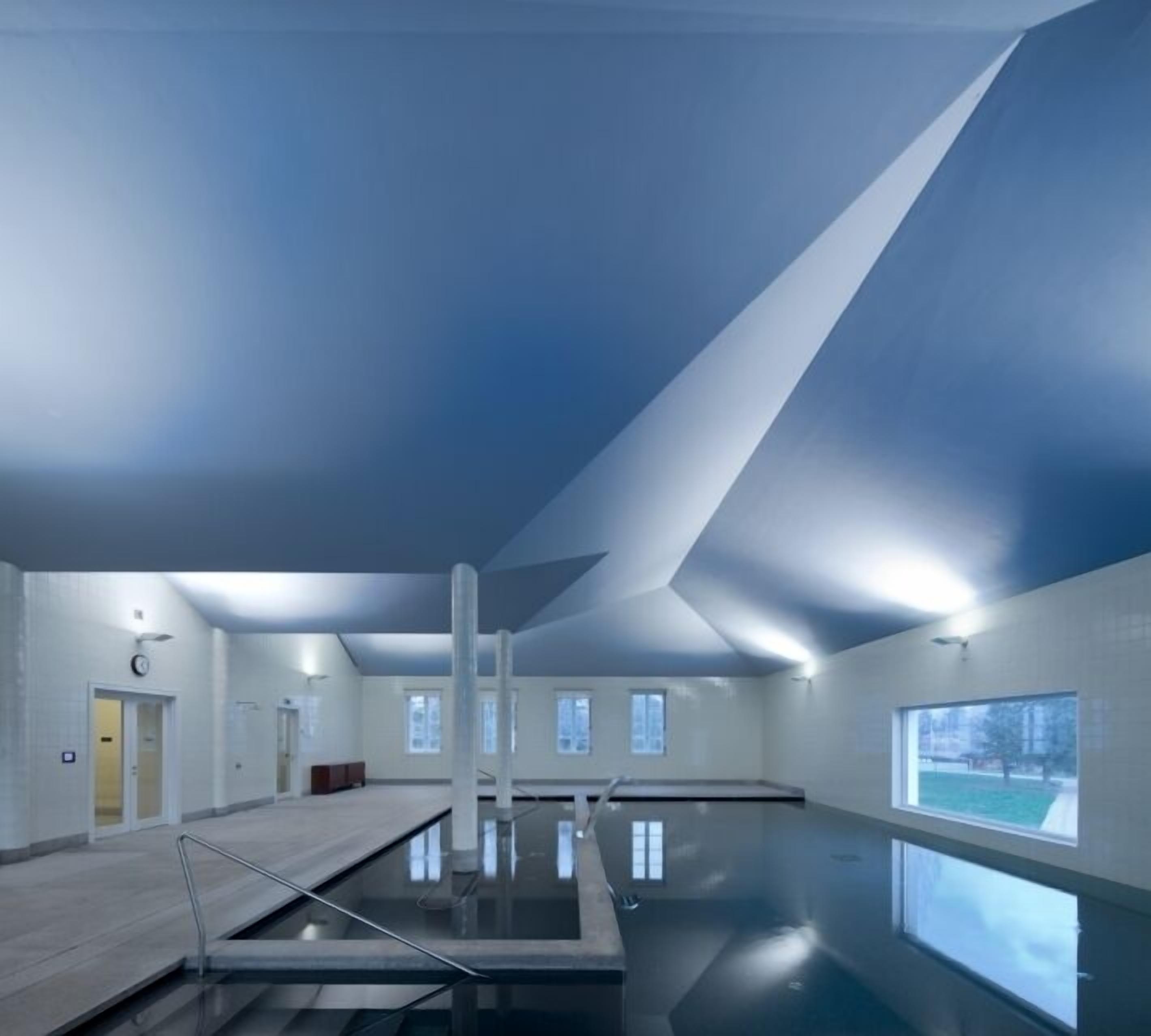 Una piscina interior con techos altos y ventanas amplias.