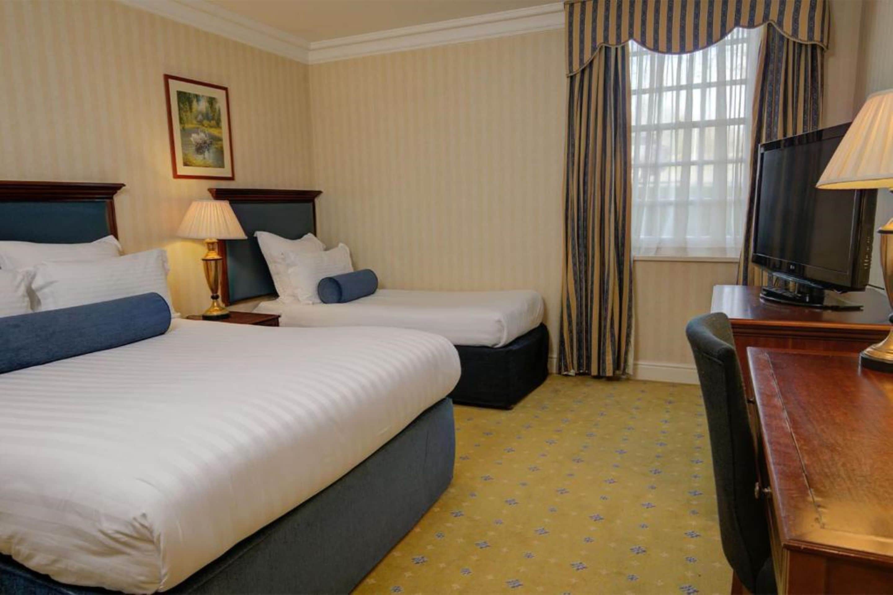 Habitación de hotel con dos camas, televisión, escritorio y ventana con cortinas.