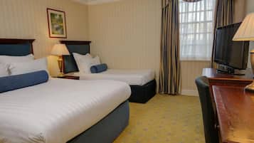 Habitación de hotel con dos camas, televisión, escritorio y ventana con cortinas.