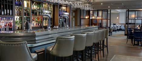 A bar area with a long counter, multiple stools, and a variety of bottles and glasses.