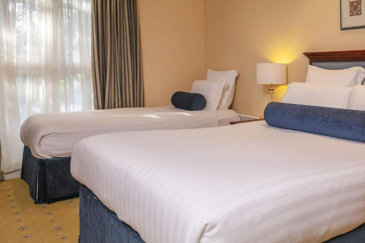 A hotel room with two beds, a lamp, and a window with curtains.