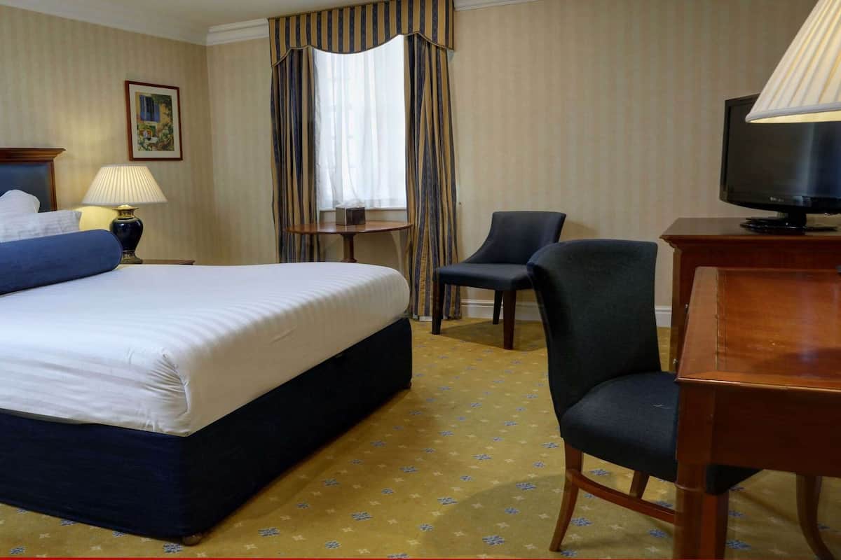A hotel room with a large bed, a desk with a lamp, a chair, and a television.