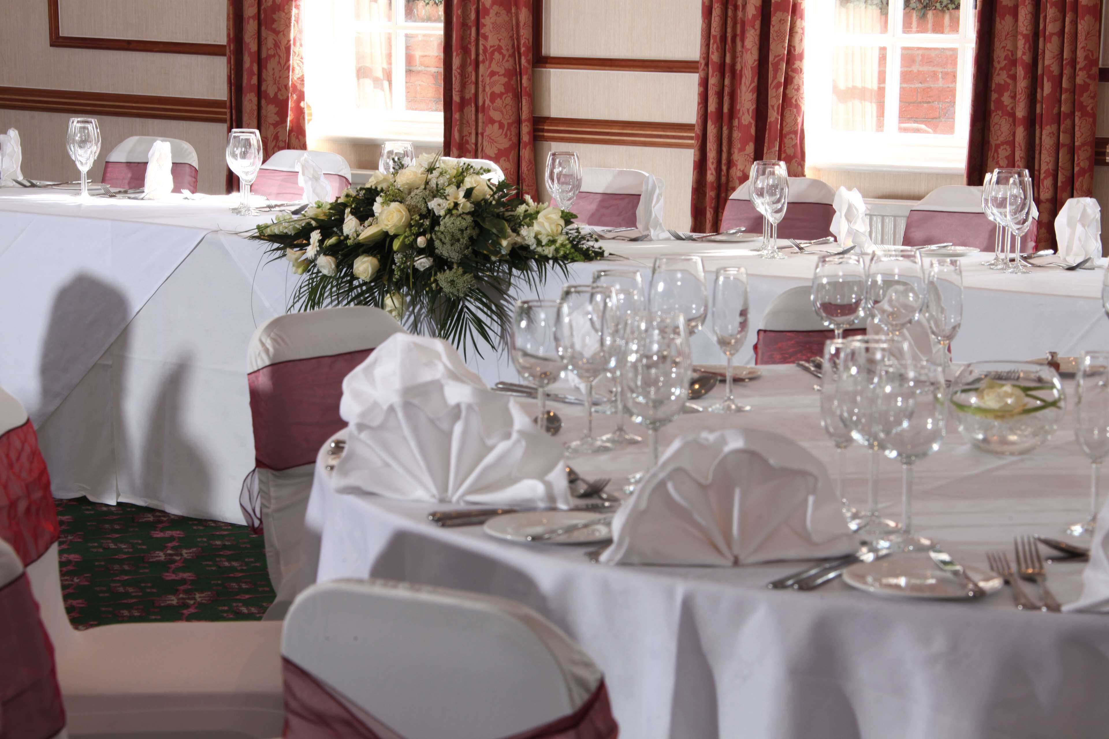 Un salón de banquetes con mesas dispuestas para un evento formal, con manteles blancos, centros de mesa florales y cubertería ordenada.