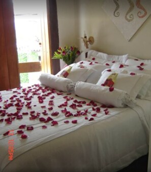 A bed with white linens and rose petals scattered across it. - Pousada do Capitão (Arraial do Cabo)