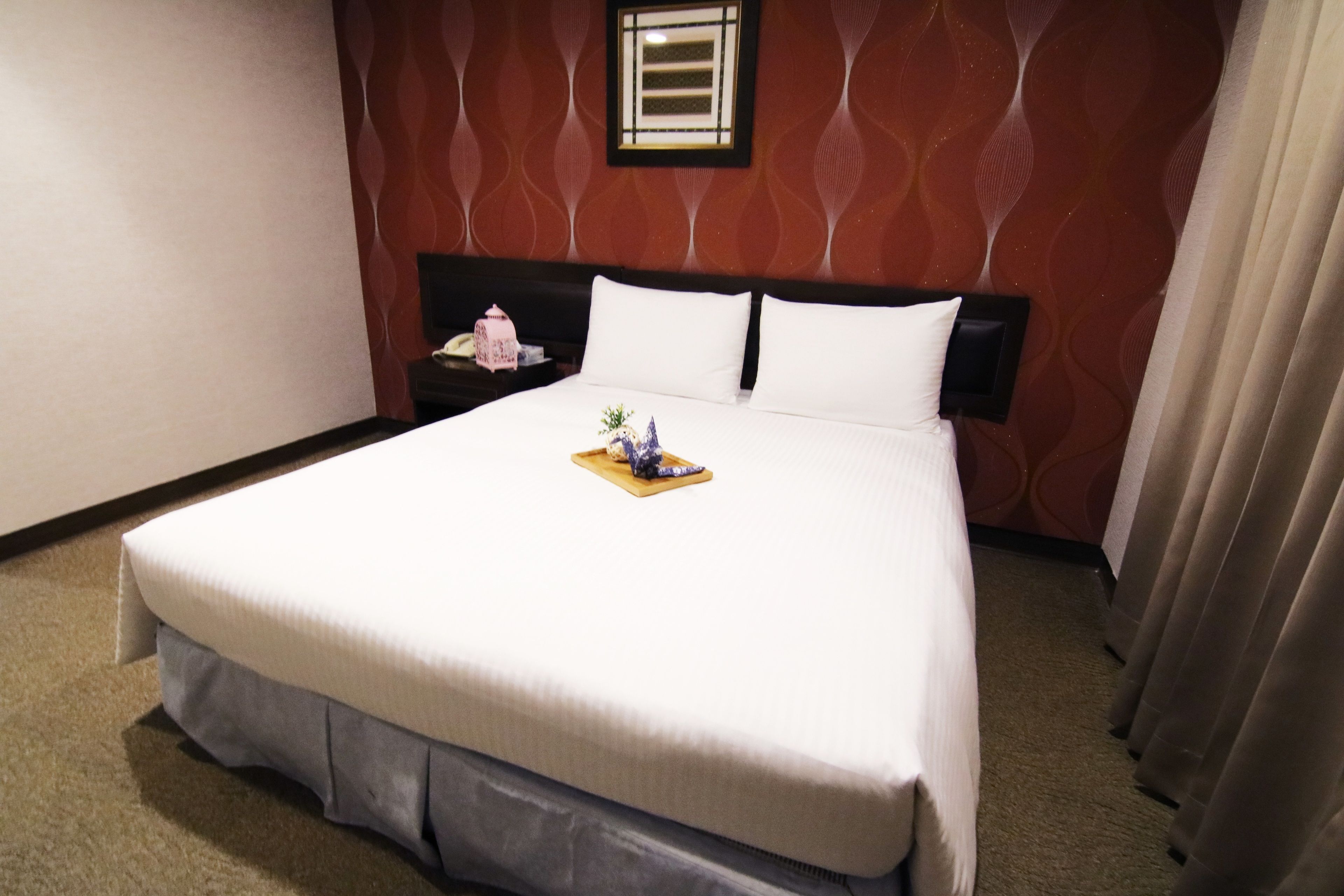 A hotel room with a large bed, a nightstand, and a wall-mounted picture frame.