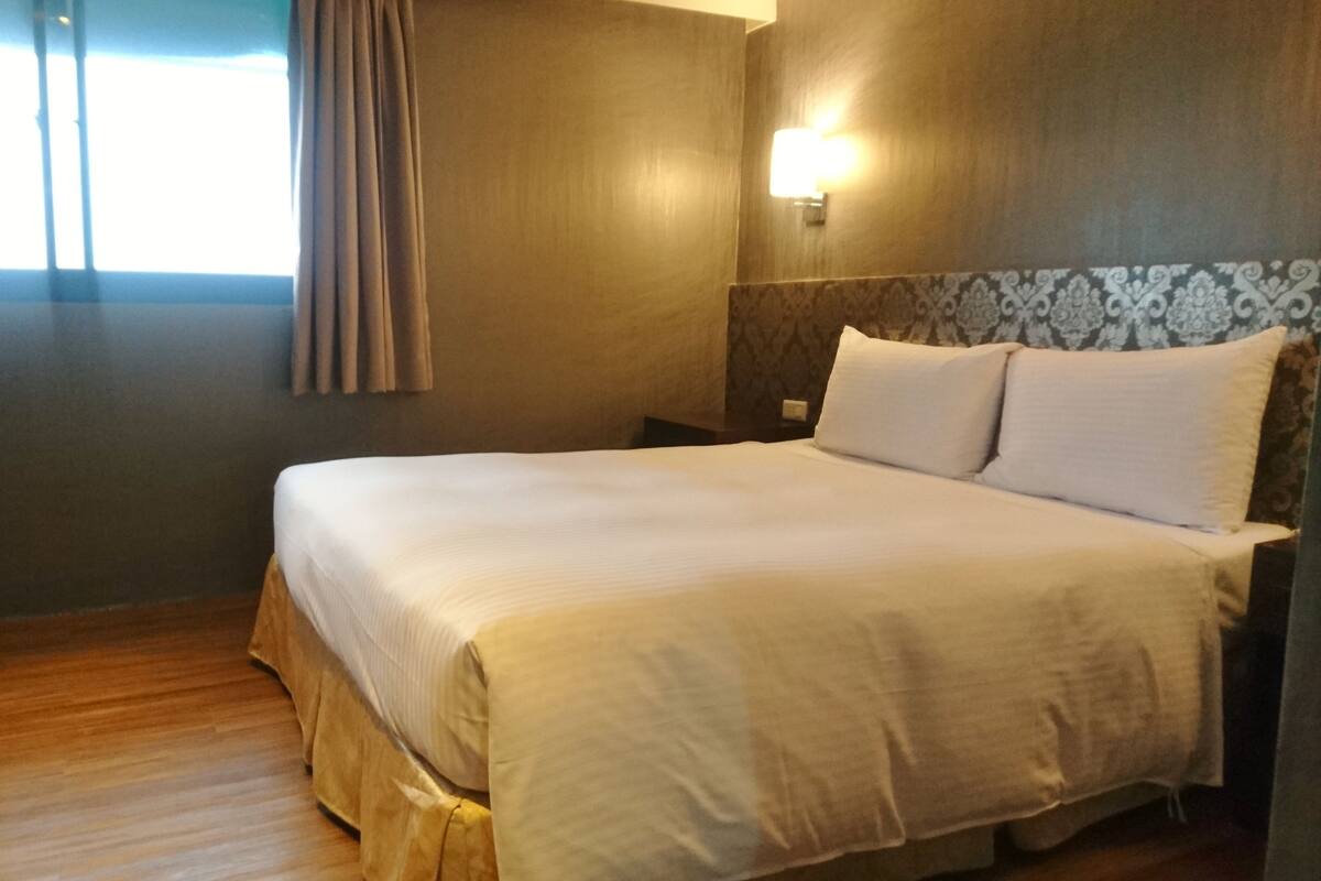 Et hotelværelse med en stor seng, trægulv, et natbord og en lampe monteret på væggen.