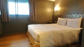 A hotel room with a large bed, wooden flooring, a nightstand, and a wall-mounted light.