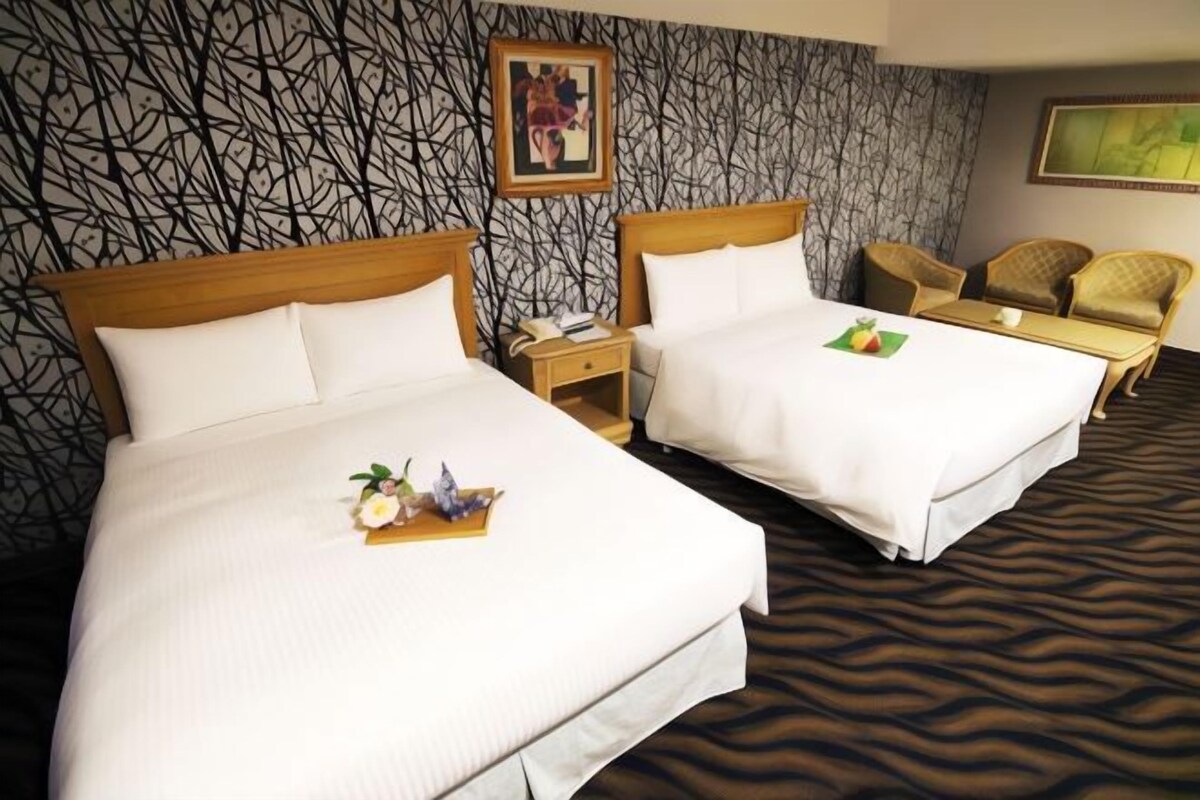 A hotel room with two beds, a wooden headboard, a patterned wall, a framed picture, and a chair.