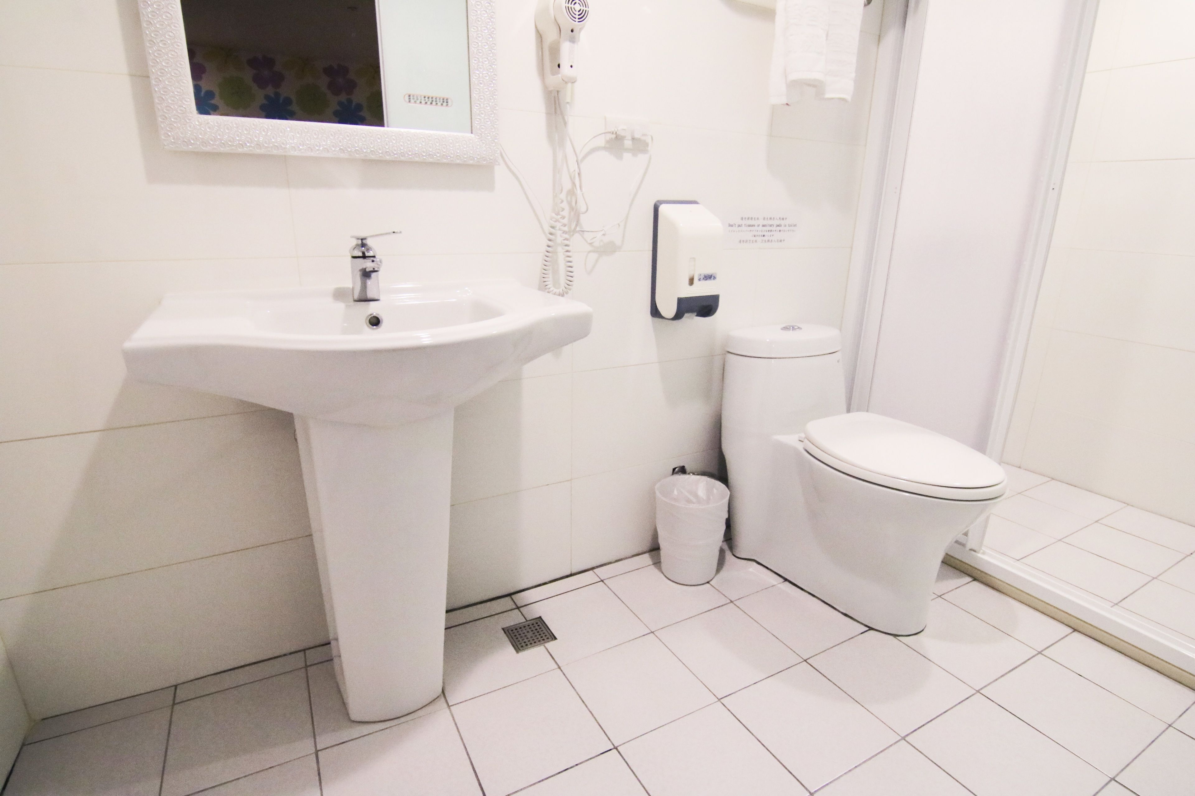 A bathroom with a white sink, toilet, and a hairdryer on the wall.