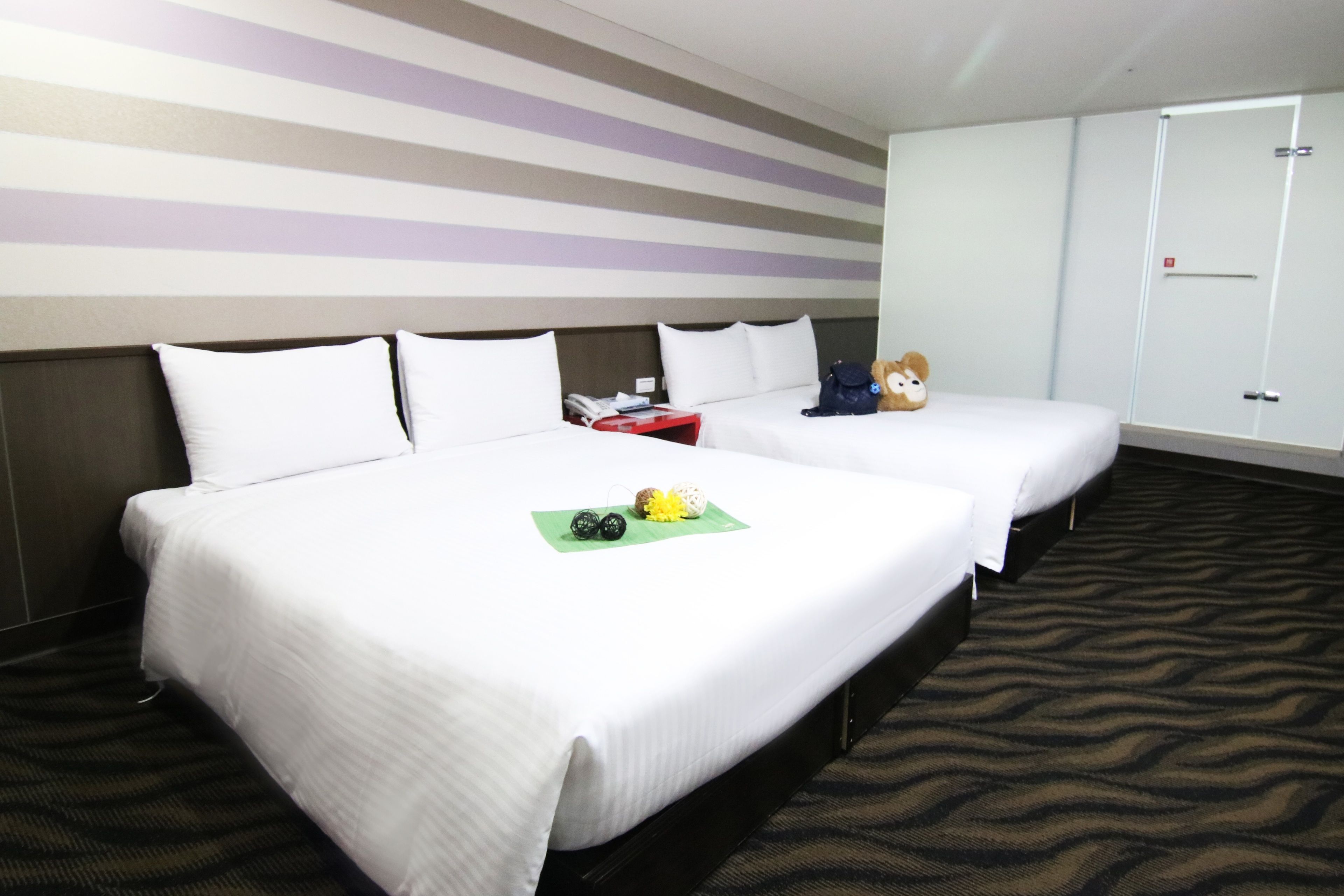 A hotel room with two beds, a striped wall, a wardrobe, and a patterned carpet.