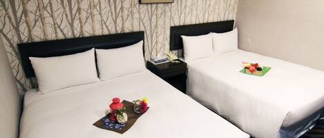 A hotel room with two beds, each with white linens and a headboard. There is a framed picture on the wall above the beds, a nightstand with a telephone, and a small table with a red lantern and flowers.