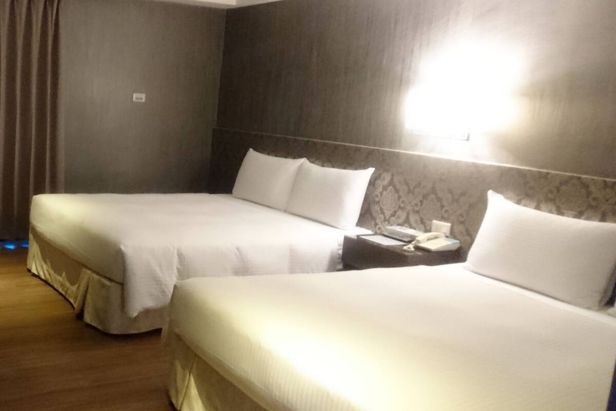 Et hotelværelse med to senge, trægulv, gardin og et natbord med en telefon.