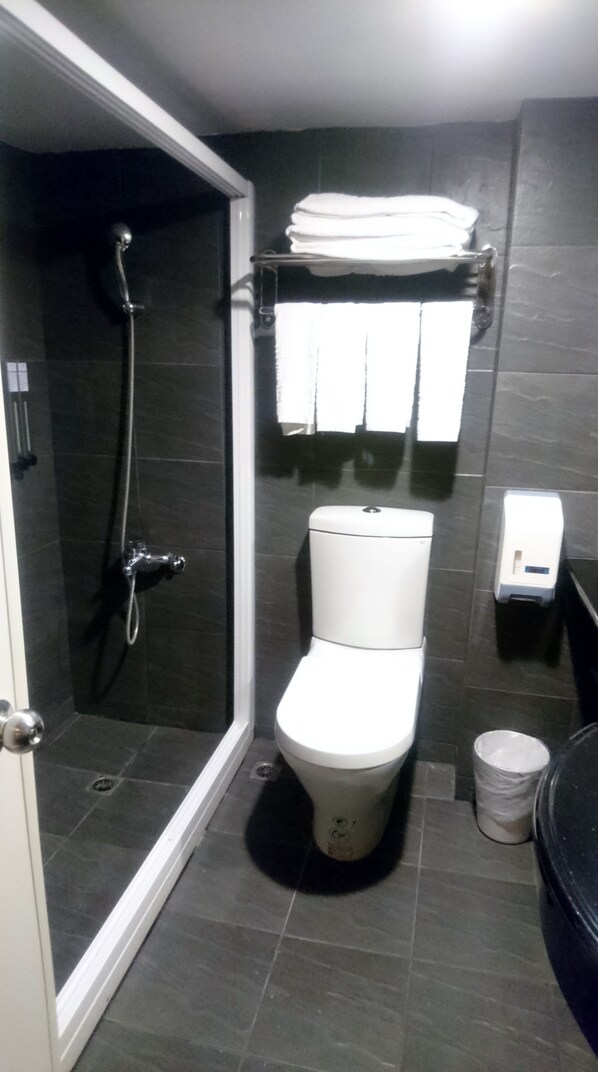 A compact bathroom with a shower, toilet, and a towel rack.