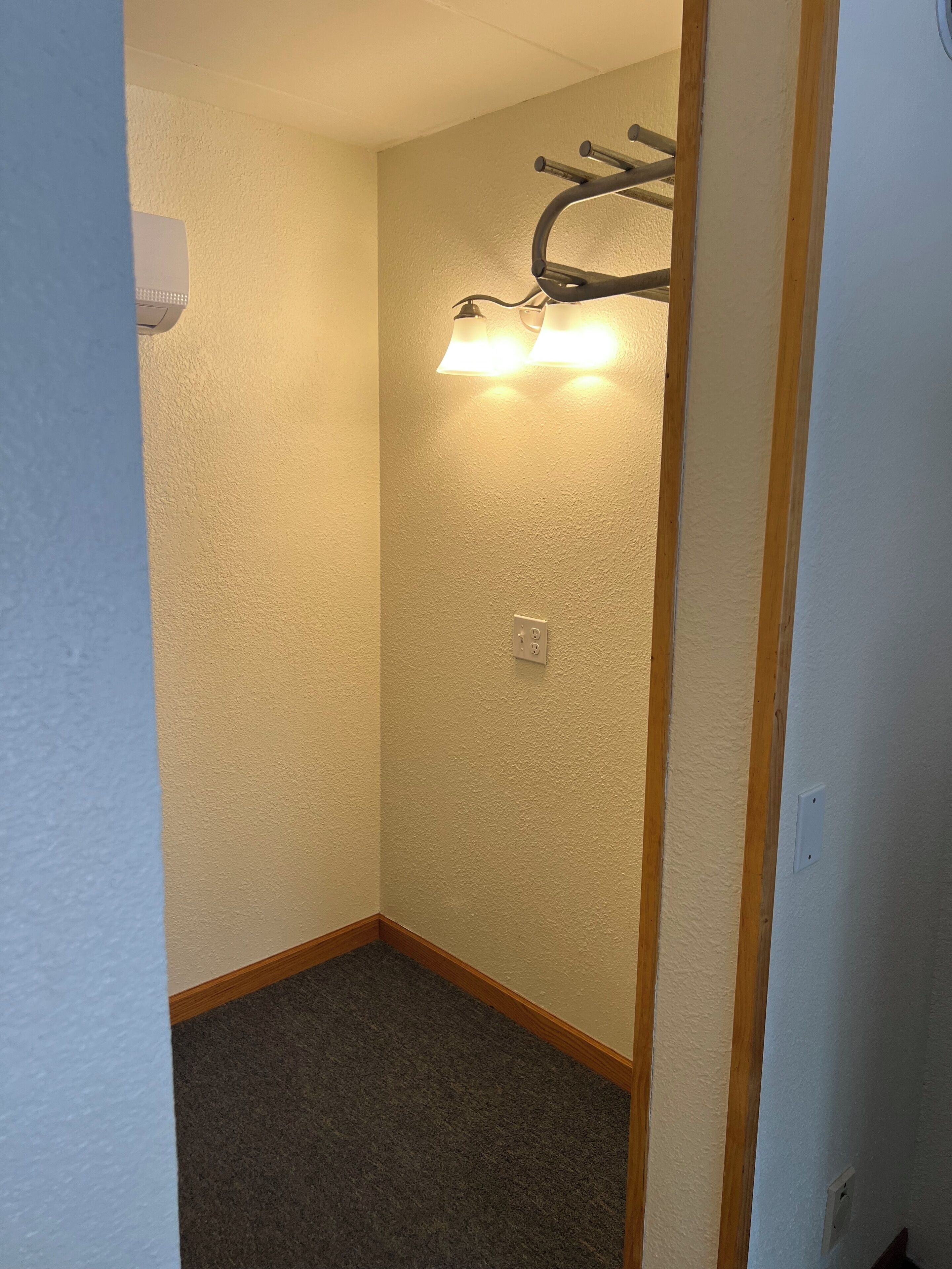 A narrow hallway with textured walls, a wooden baseboard, and a wall-mounted light fixture.