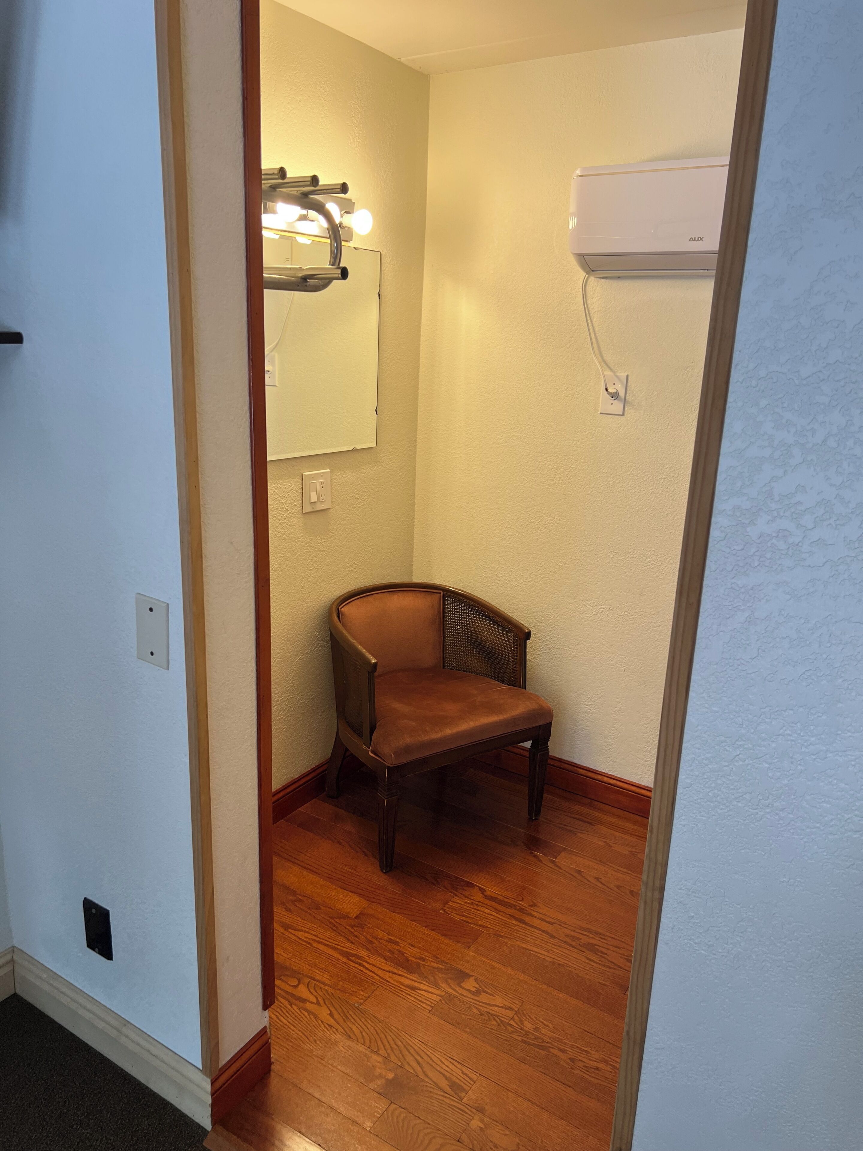 Un couloir étroit doté d’un plancher en bois, d’une chaise marron, d’un luminaire fixé au mur et d’un appareil de climatisation.