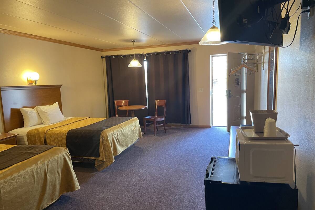 A hotel room with two beds, a desk, a chair, a television, and a microwave.