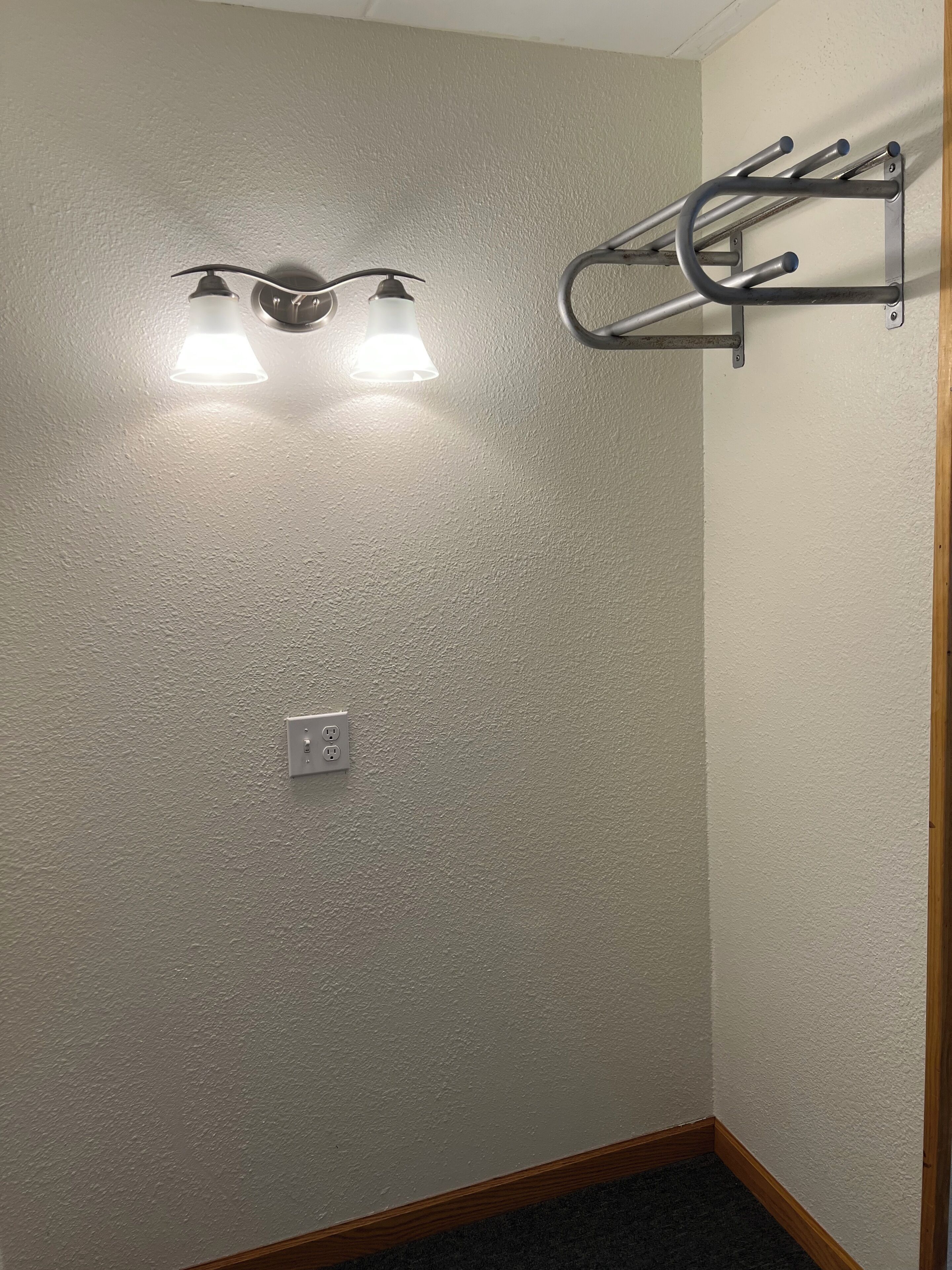 A bathroom with a textured wall, a light fixture, a towel rack, and a wooden baseboard.