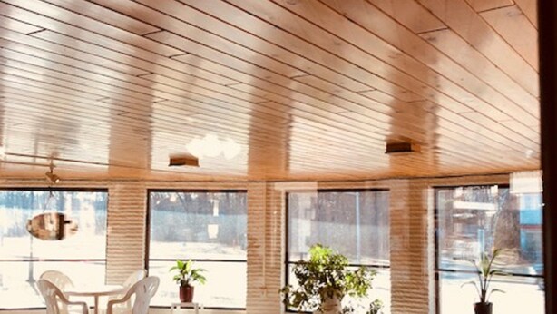 A modern indoor pool area with wooden ceiling beams, large windows, and a seating area with chairs and potted plants. - Amber's Inn & Suites (Wisconsin Dells)