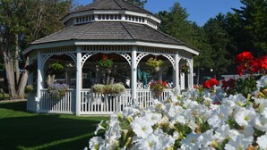 A white gazebo with a rounded roof, surrounded by lush greenery and white flowers. - Amber's Inn & Suites (Wisconsin Dells)