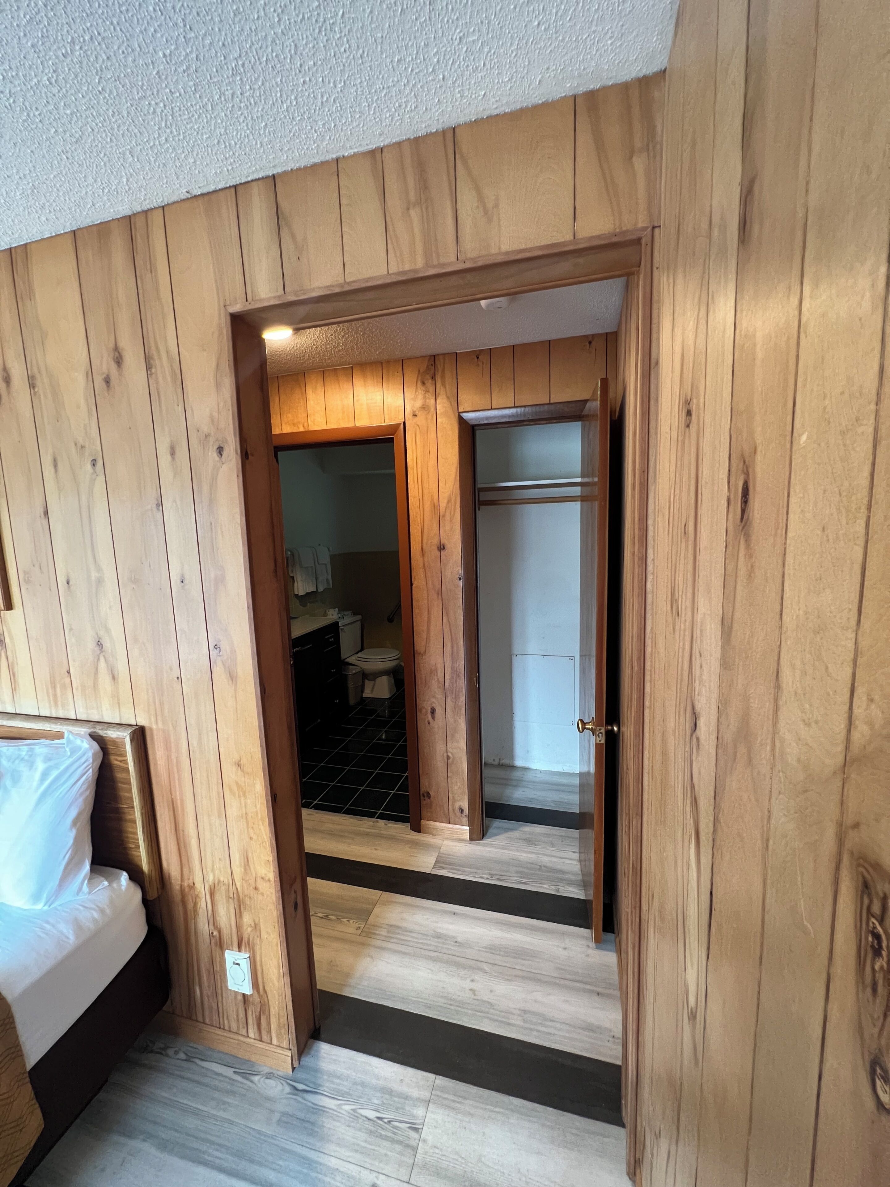 A wooden-paneled room with a bed, a door leading to a bathroom, and a tiled floor.