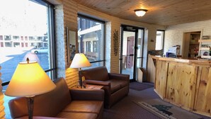 A cozy room with leather sofas, a wooden reception desk, and large windows offering a view of the outside. - Amber's Inn & Suites (Wisconsin Dells)