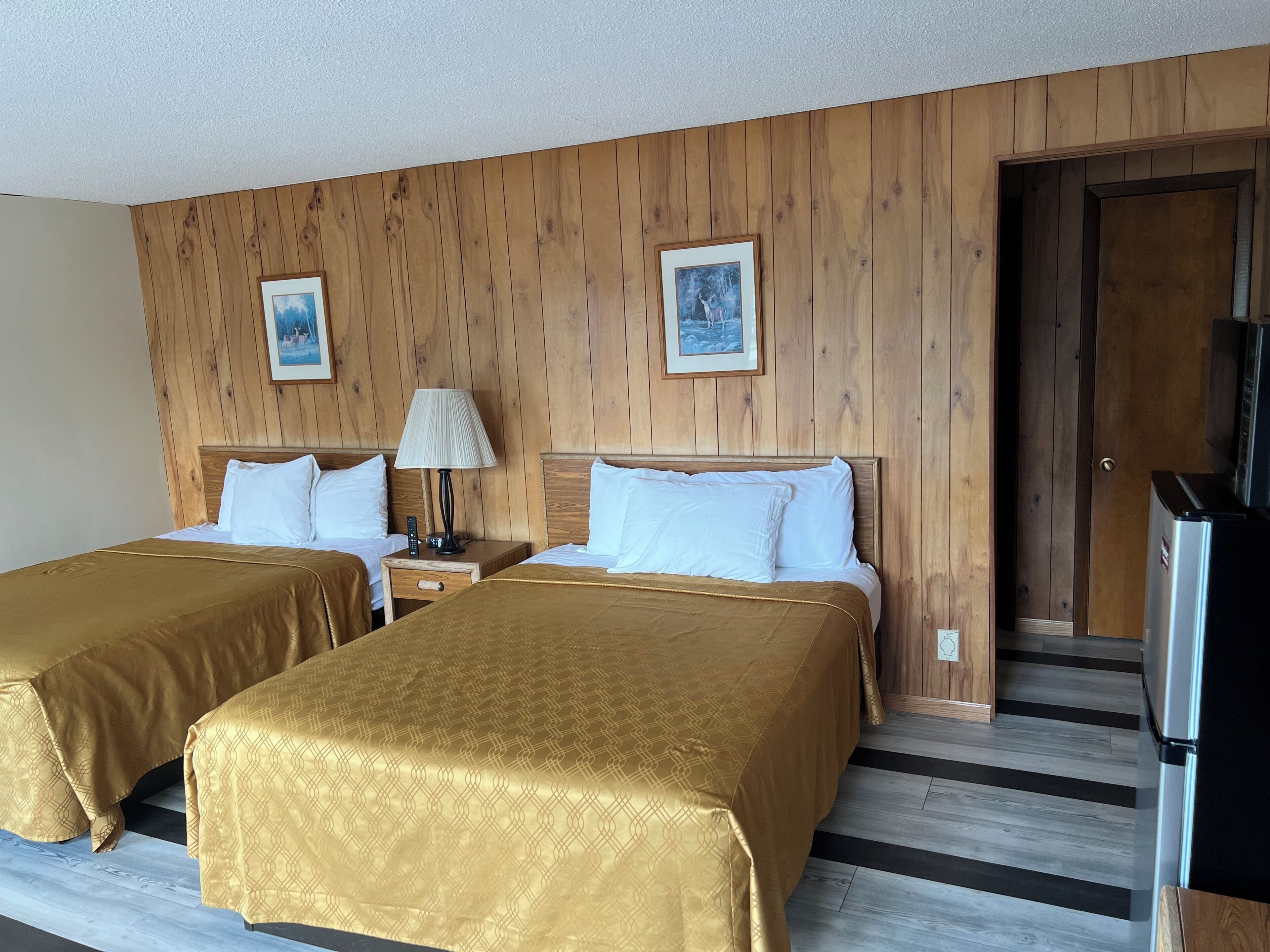Een hotelkamer met twee bedden, houten paneelwanden, een koelkast en twee ingelijste foto's.