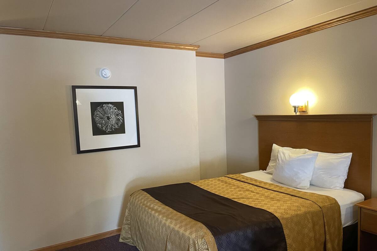 A hotel room with a bed, a framed picture on the wall, and a nightstand with a lamp.
