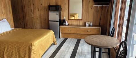 A hotel room with a bed, a small kitchenette, a dining table with a chair, and a TV mounted on the wall.