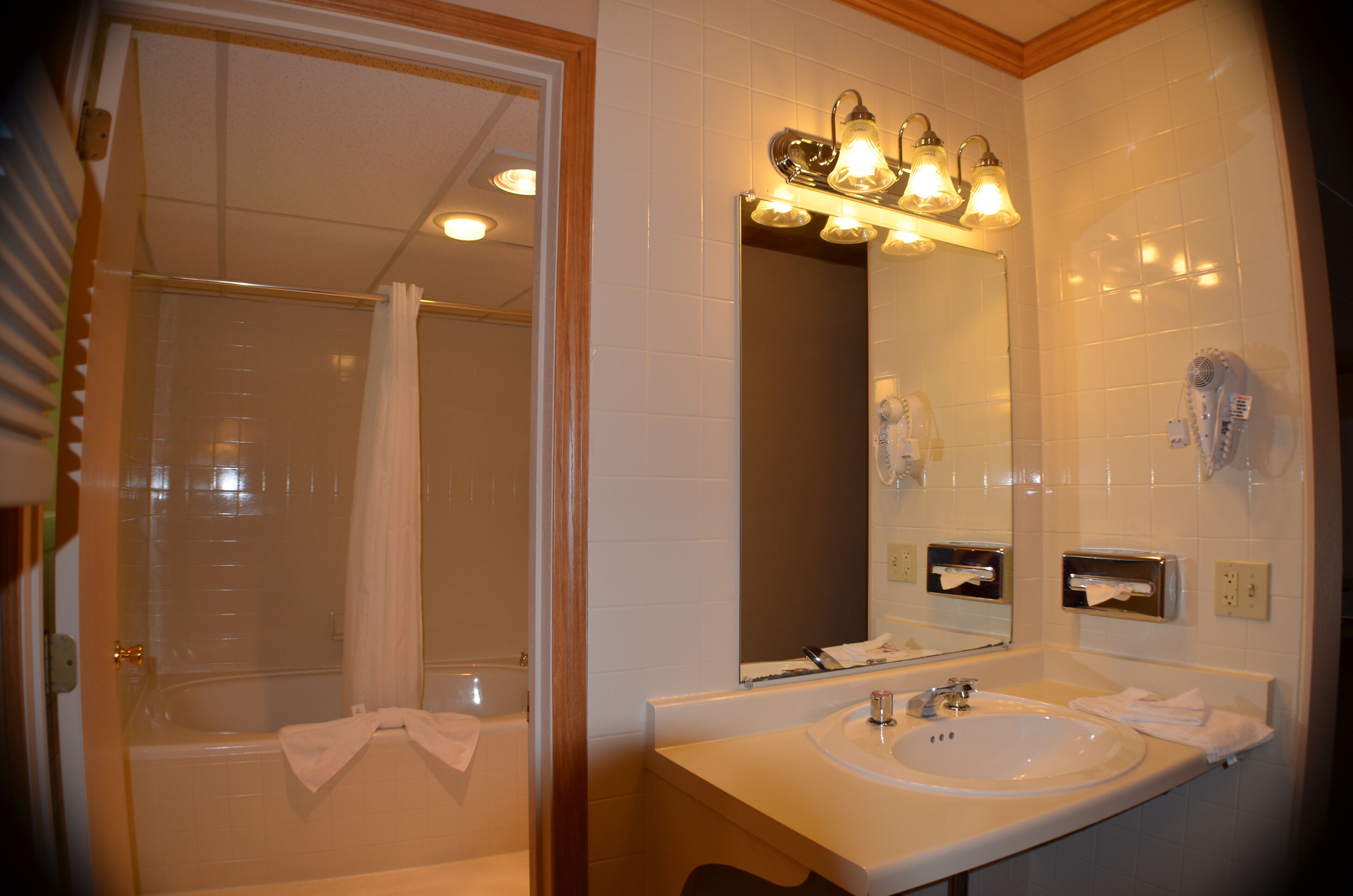 A bathroom with a bathtub, a sink, a mirror, and a hairdryer on the wall.