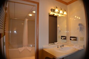A bathroom with a bathtub, a sink, a mirror, and a hairdryer on the wall.