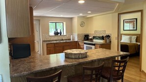 A kitchen with a central island, wooden cabinets, and a dining area with chairs. - Amber's Inn & Suites (Wisconsin Dells)