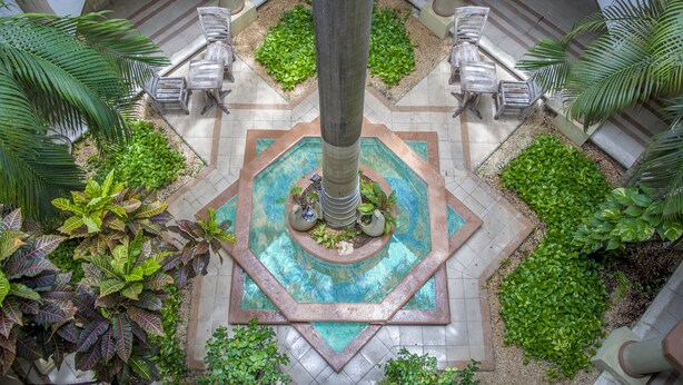 Une cour intérieure avec une fontaine centrale, entourée de plantes en pot et d’espaces aménagés pour s’asseoir.