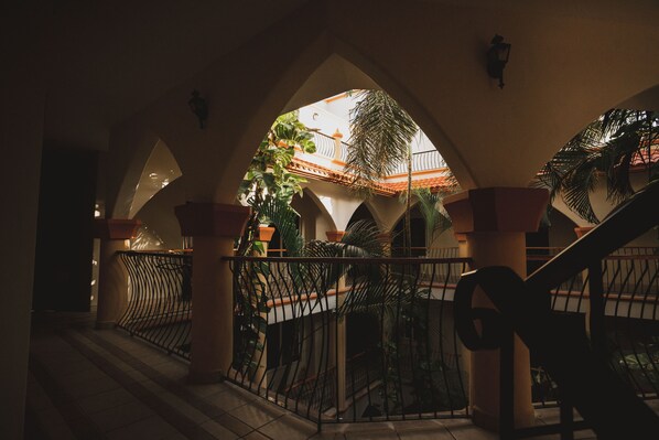 Un patio interior con suelo de baldosas, barandilla de metal y una escalera.