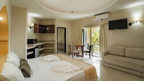 Une chambre d’hôtel comprenant un lit, un canapé, un coin repas avec des chaises, un téléviseur fixé au mur et un appareil de climatisation.