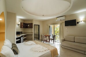 A hotel room with a bed, a sofa, a dining area with chairs, a TV mounted on the wall, and an air conditioning unit. - Sahara Hotel (Playa del Carmen)