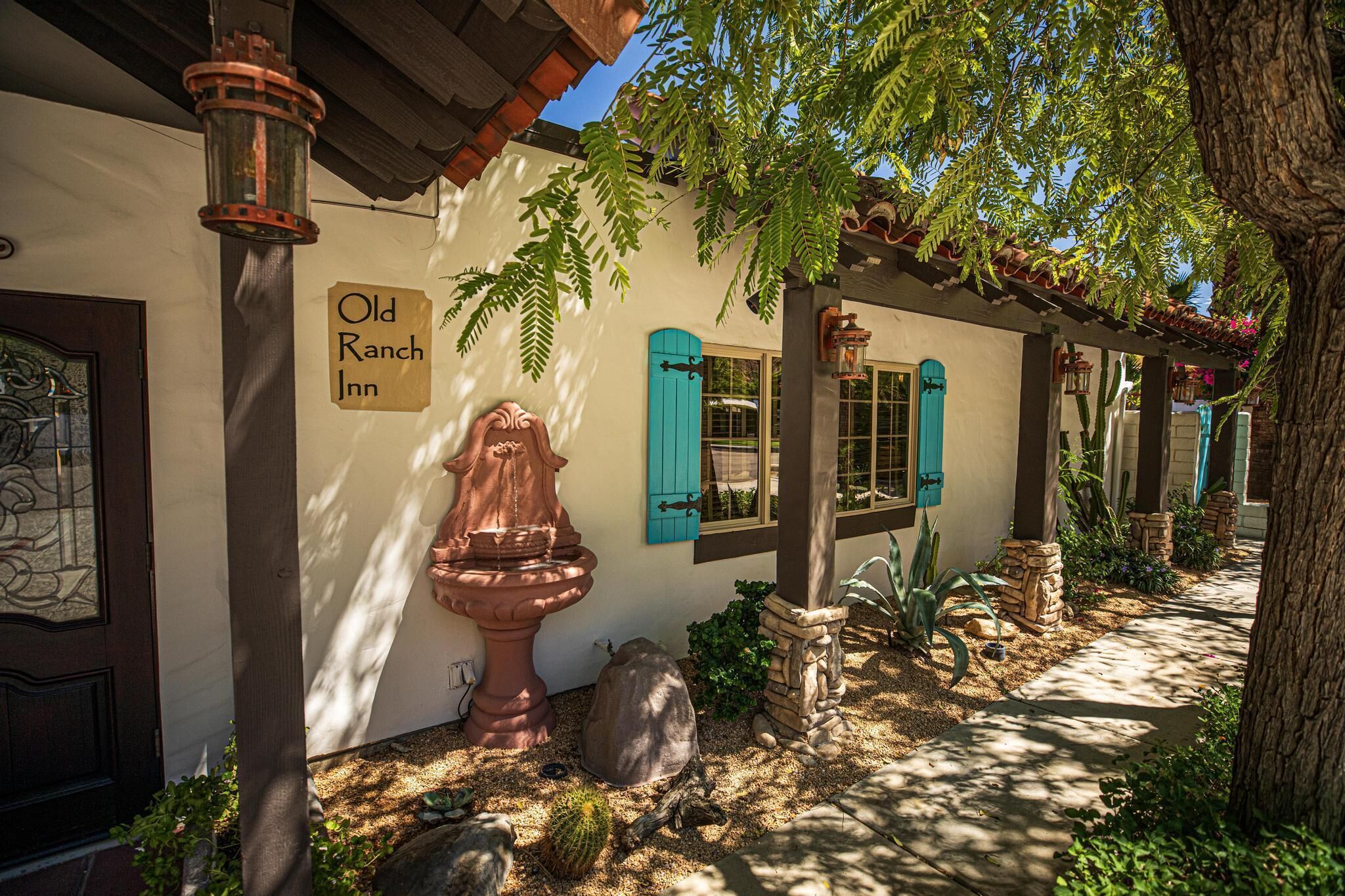 A building with a sign reading "Old Ranch Inn," a large planter, and a stone pillar.