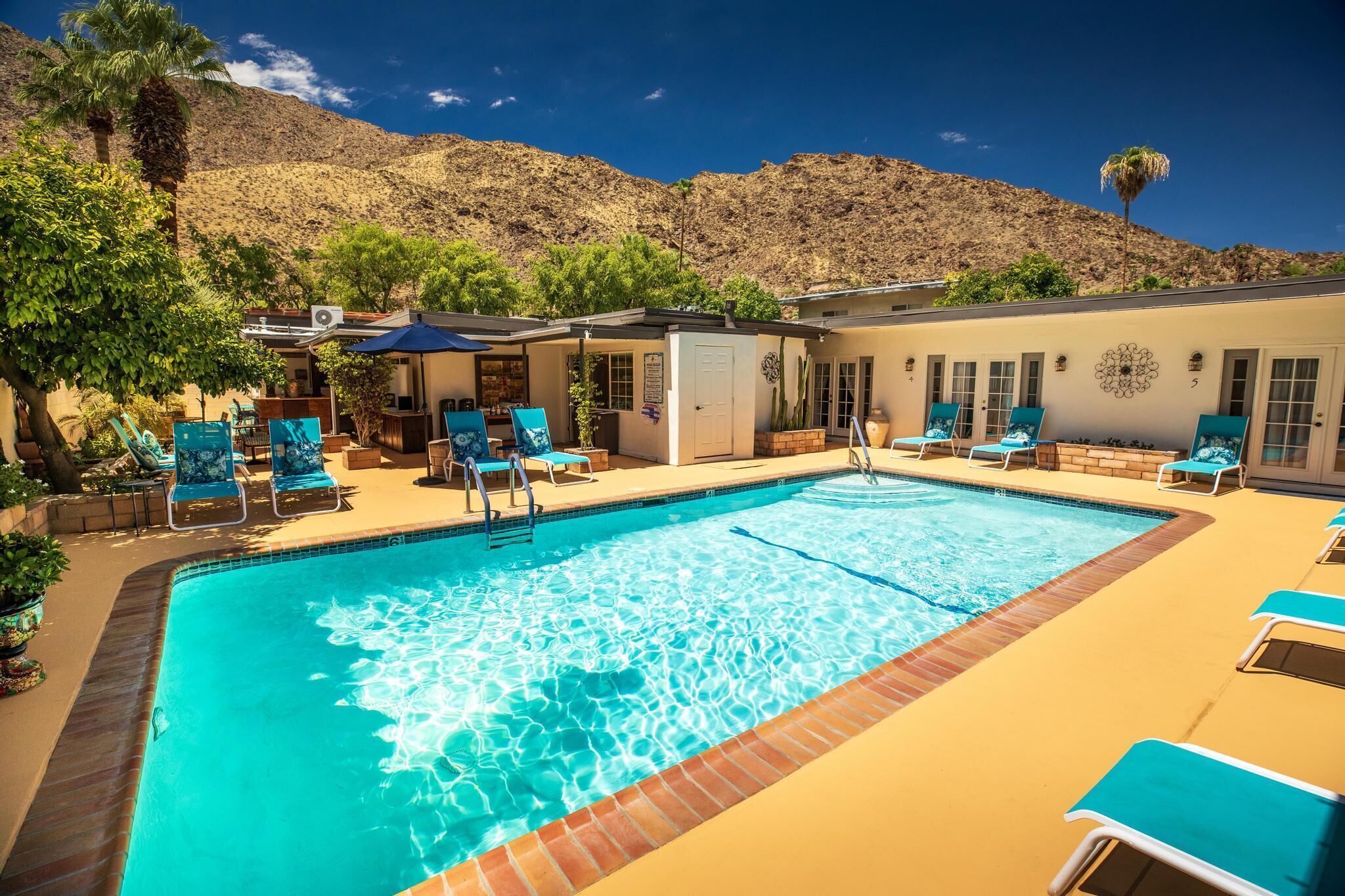 A swimming pool with lounge chairs, a covered seating area, and a mountain backdrop.