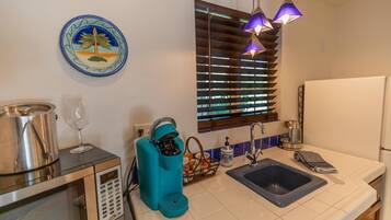 A compact kitchen with a microwave, coffee maker, sink, and a decorative plate on the wall.