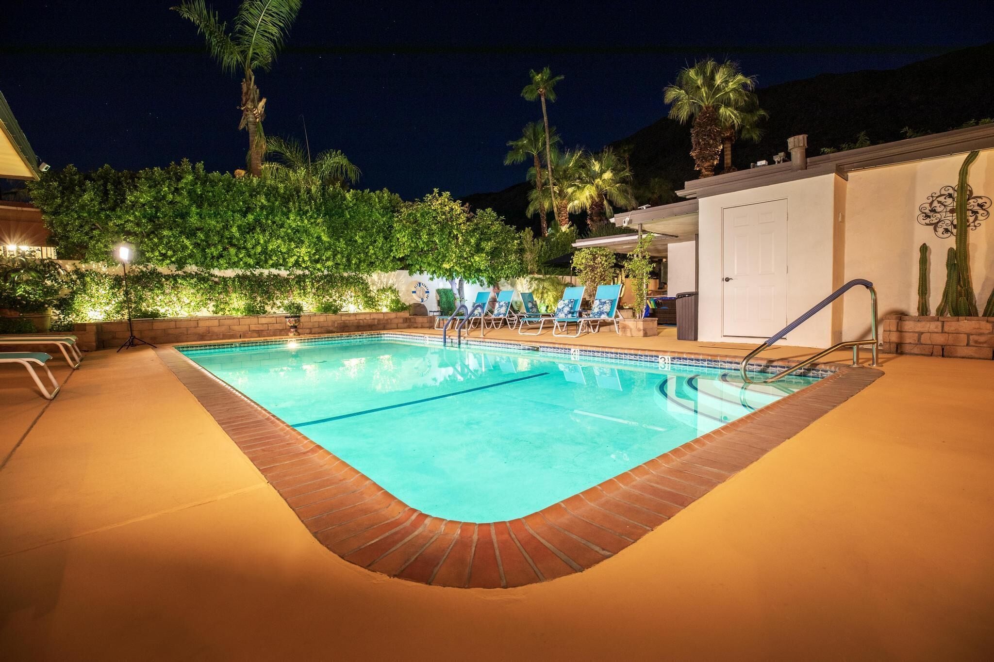 A swimming pool with lounge chairs, palm trees, and a building in the background.