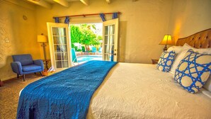 A bedroom with a large bed, a chair, a lamp, and a view of an outdoor pool area. - Old Ranch Inn - Adults Only  (Palm Springs)