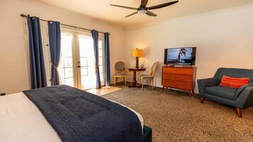 Een hotelkamer met een bed, een bureau met lamp, een televisie, een stoel en een plafondventilator.